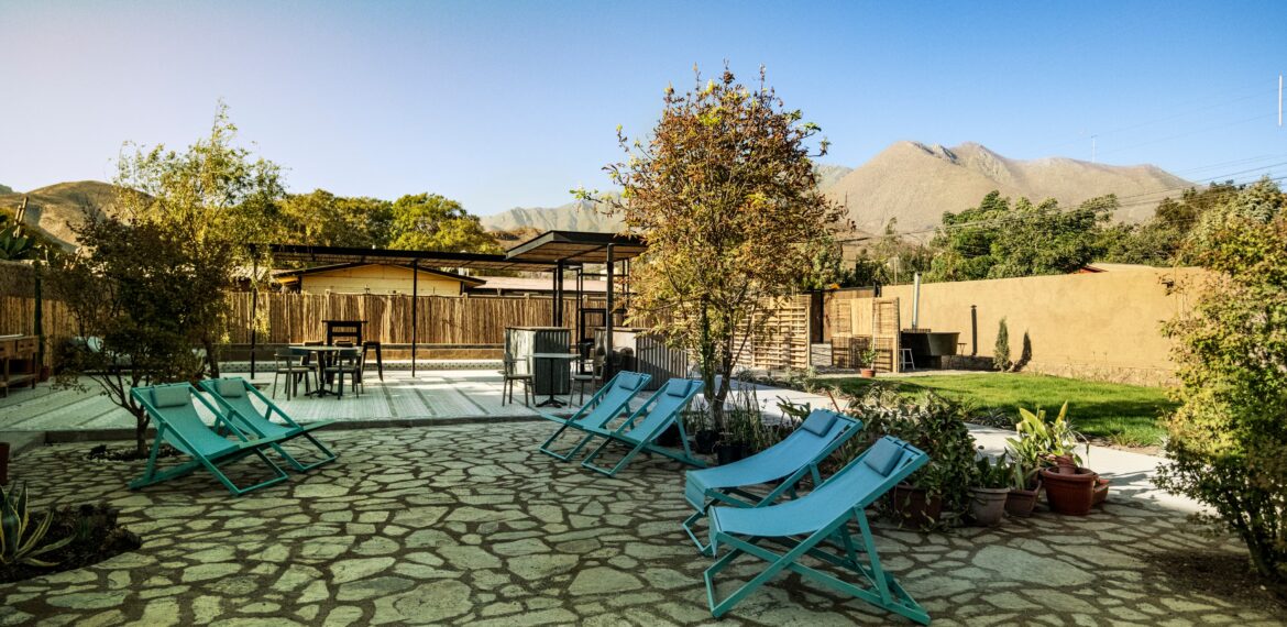 Patio exterior con reposeras azules, árboles y piso de piedra, rodeado de naturaleza y montañas al fondo