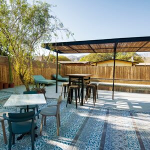 Terraza exterior con piscina, sillas y mesas bajo pérgola, rodeada de árboles y cercos de bambú, ambiente tranquilo y natural