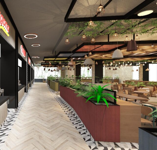 Vista de un pasillo con locales de comida rápida y área de mesas, con decoración moderna, plantas y luminarias colgantes, en un ambiente amplio y luminoso.