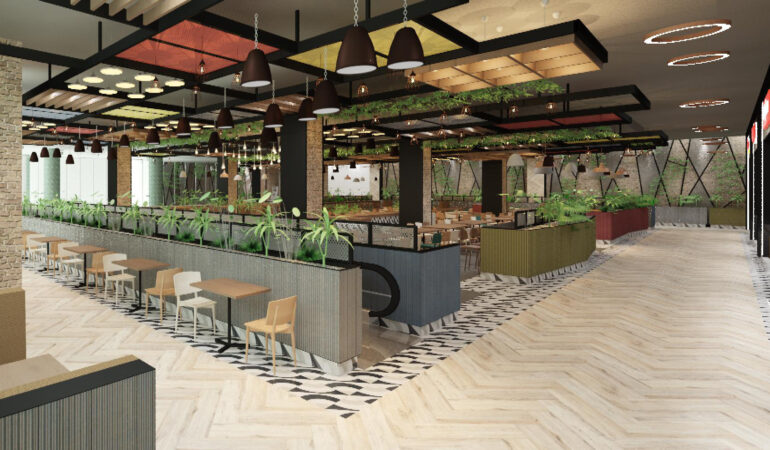 Food court amplio y moderno con mesas, sillas, plantas decorativas y luminarias colgantes, mostrando un diseño contemporáneo con detalles naturales y una escalera mecánica en el centro.