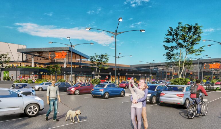 Imagen del estacionamiento del centro comercial Espacio Urbano, con vehículos estacionados, personas paseando, ciclistas y familias disfrutando de un día soleado frente a la fachada del mall.