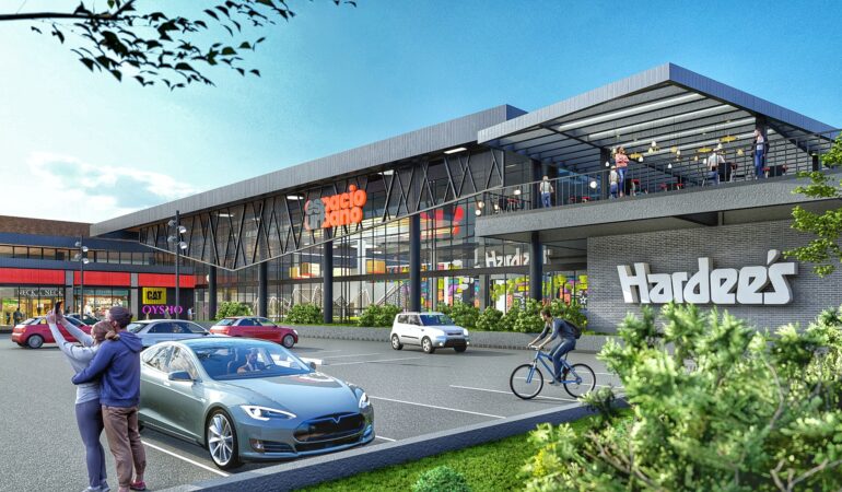 Vista exterior del centro comercial Espacio Urbano con el restaurante Hardee’s en primer plano, personas tomándose selfies, ciclistas y autos estacionados en el sector del acceso principal.