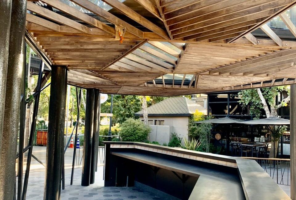 Detalle de barra de centro comercial al aire libre, con techo de madera de diseño geométrico y piso de baldosas hexagonales.