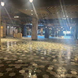 Vista amplia de un área interior remodelada en Espacio Urbano con piso de mosaico hexagonal, columnas revestidas en madera y techos con diseño moderno e iluminación cálida.