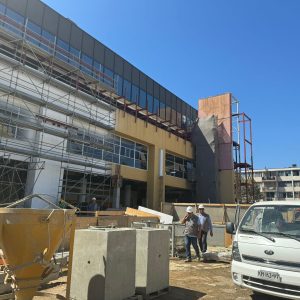 Fachada del centro comercial Espacio Urbano Las Rejas en proceso de construcción, con andamios metálicos, trabajadores con casco y camioneta blanca en primer plano bajo cielo despejado.