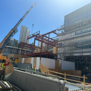 Construcción con grúa, estructura metálica, andamios y trabajadores en faena.