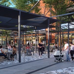 Personas compartiendo en una terraza al aire libre del centro comercial Espacio Urbano 15 Norte, con mesas distribuidas bajo pérgolas metálicas, rodeadas de árboles, plantas colgantes y un entorno moderno y natural.