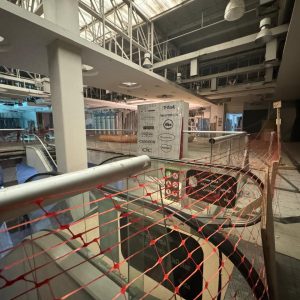 Vista del segundo piso de un centro comercial en remodelación, con escaleras mecánicas fuera de servicio y cercado de seguridad en color naranja delimitando el área