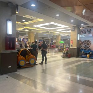 Área iluminada de centro comercial con juegos mecánicos infantiles y local de postres de McDonald’s; personas transitando por el pasillo.